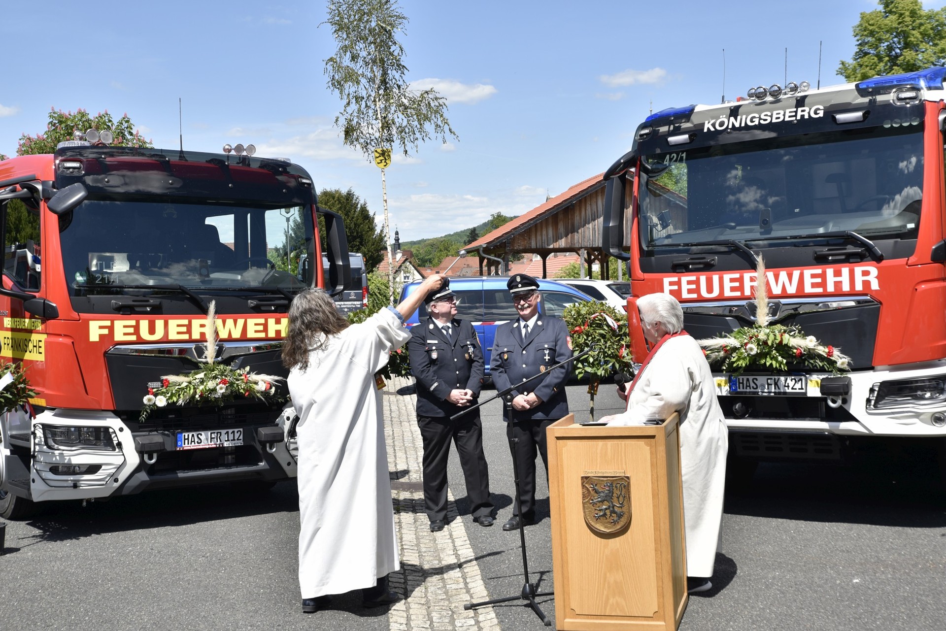 Pastoralreferentin Claudia Nowak (links) und Diakonin Sabine Dresel (rechts) segneten in ökumenischer Eintracht die beiden neuen Fahrzeuge. Aufmerksame Beobachter der Kommandant Stefan Burkard vor dem Fahrzeug der Werkfeuerwehr FRÄNKISCHE (links) und KBM und Kommandant Peter Schüler vor dem Fahrzeug der FF Königsberg (rechts)